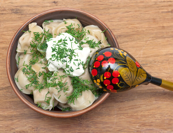 Русские пельмени в глиняной миске со сметаной и укропом на вазе
