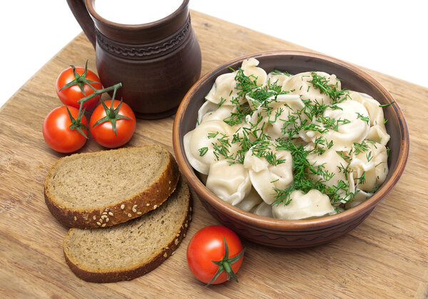 Русские пельмени, хлеб и помидоры черри на разделочной доске
