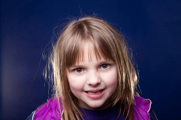 工作室拍摄了一个年轻的金发女孩在蓝色背景下做傻脸的照片 — 图库照片
