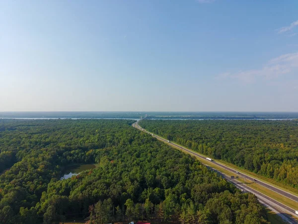Her iki tarafında ağaçlar ve açık mavi bir gökyüzü olan bir yol. Yol boş ve üzerinde hiç araba yok.