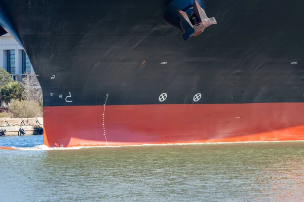 Güneşli bir günde dar bir kanalda giden büyük bir konteynır gemisinin pruvası.