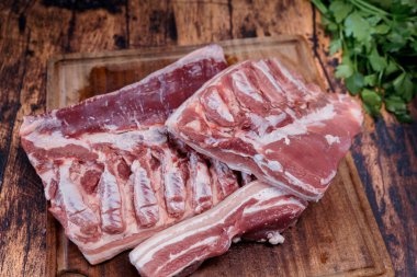 Eski ahşap bir masada duran kullanılmış bir kesme tahtasının üzerinde taze domuz göbeği.