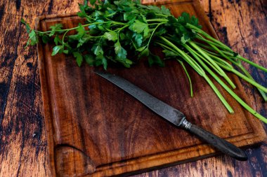 Üzerinde bıçak ve maydanoz olan eski ahşap bir masanın üzerinde aşınmış tahta kesme tahtası.