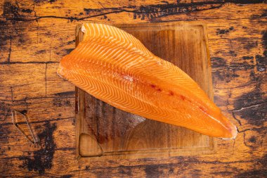 Büyük çiğ somon filetosu. Tahtada balık kemiği pensesi var.