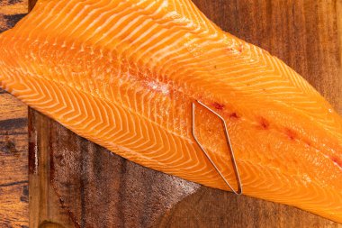 Büyük çiğ somon filetosu. Tahtada balık kemiği pensesi var.
