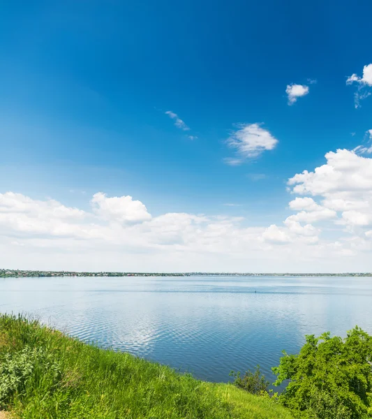 Deep blue sky with clouds over river and green grass — Stock Photo, Image