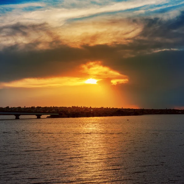 Πορτοκαλί ηλιοβασίλεμα στον δραματικό ουρανό και το ποτάμι με την γέφυρα — Φωτογραφία Αρχείου