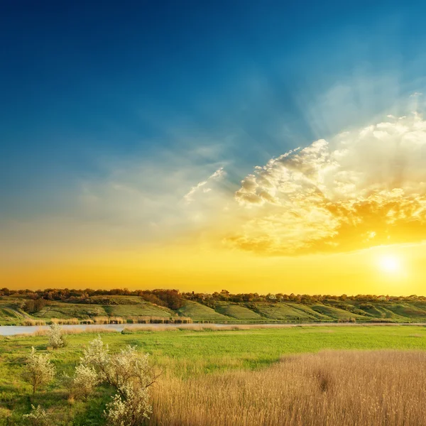 Hellen Sonnenuntergang über Fluss und grünen Seiten — Stockfoto