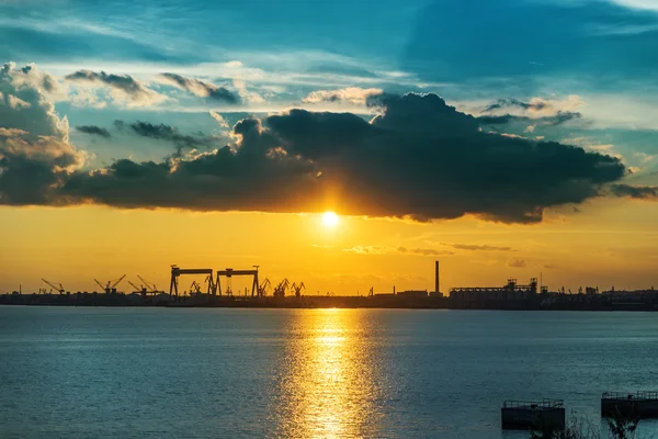 Pôr do sol em nuvens escuras ao longo do rio e da construção naval da fábrica — Fotografia de Stock