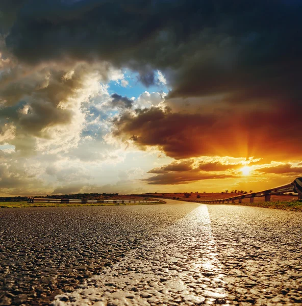 Baixa por do sol laranja em nuvens dramáticas sobre a estrada de asfalto — Fotografia de Stock