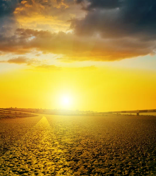 Pôr do sol amarelo, com nuvens negras sobre a estrada de asfalto — Fotografia de Stock