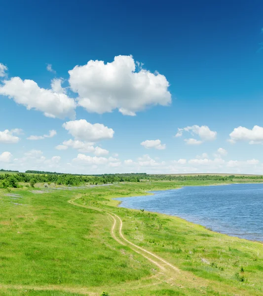 Grönt landskap med väg och damm under blå himmel med vita clo — Stockfoto