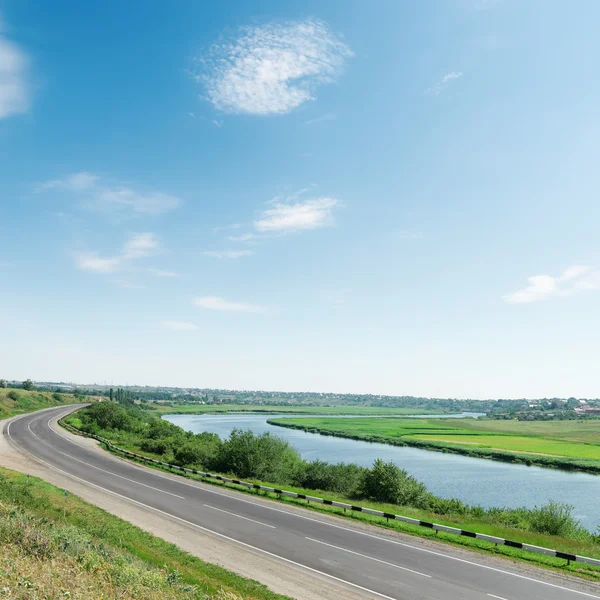 Carretera asfaltada a lo largo del río y el azul cielo sobre ella —  Fotos de Stock