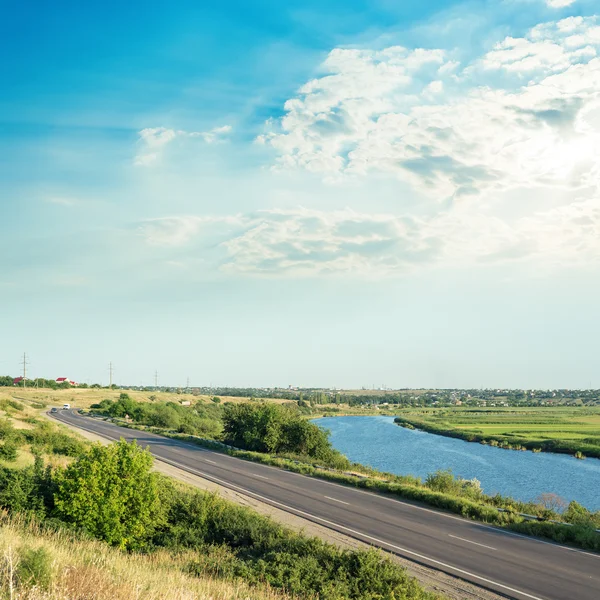 Puesta de sol en las nubes sobre el río y el asfalto de la carretera —  Fotos de Stock