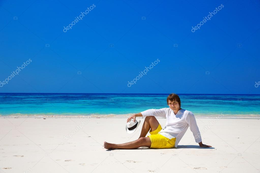 Successful handsome man in hat resting on exotic seashore with b