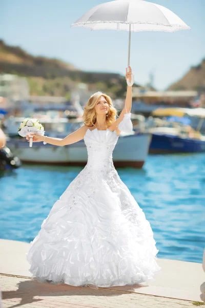 Schöne Braut im Brautkleid mit weißem Regenschirm posiert über — Stockfoto