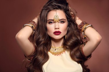 Uzun dalgalı saç stili ve parlak makyajlı güzel bir kadın. Kundan altın mücevher seti ile genç Hindu esmer model kahverengi stüdyo arka planda izole. 