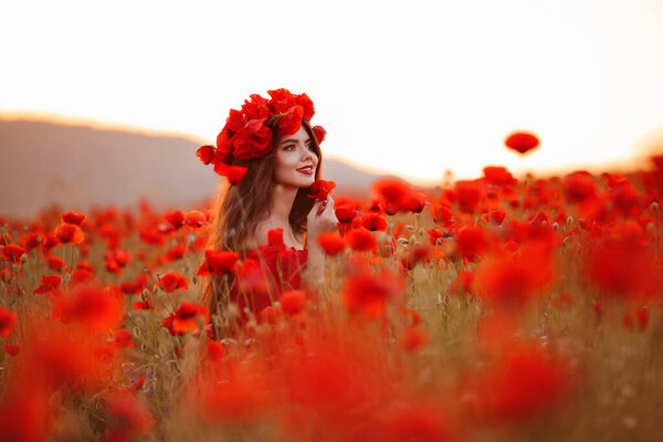 Beautiful brunette in red poppies field. Happy smiling teen girl portrait with wreath on head enjoying in poppy flowers nature background. Carefree woman.