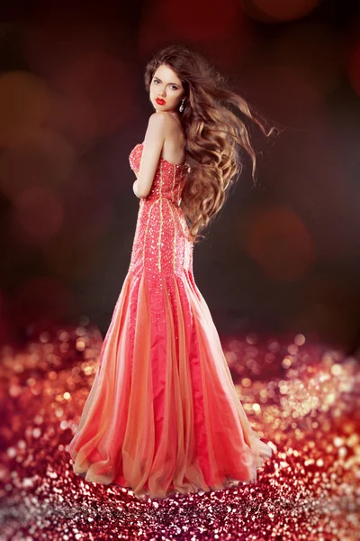 Krásný glam s dlouhými vlasy pózuje v červených šatech nad bokeh bri — Stock fotografie