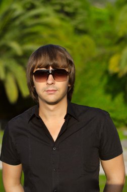 Genç yakışıklı adam açık havada dikey. Son moda erkek güneş gözlüğü 