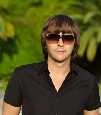 Genç yakışıklı adam açık havada dikey. Son moda erkek güneş gözlüğü 