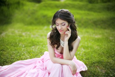 : S yeşil çimenlerin üzerinde oturan çekici esmer genç gelin kız