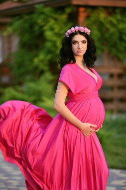 Beautiful pregnant woman touching her belly wearing in pink dres