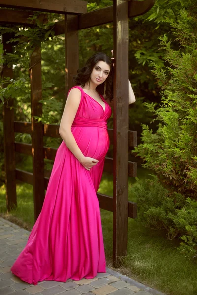 Красивая беременная женщина в розовом платье в зеленом парке — стоковое фото