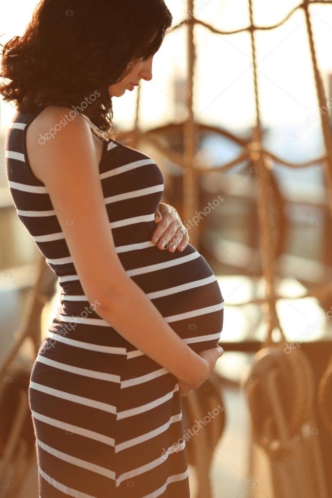 Beautiful pregnant woman touching her belly on the ship at sunse
