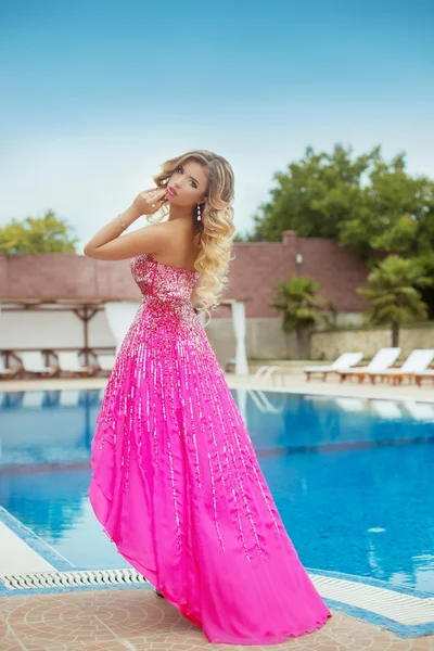 Beautiful girl model in pink fashion dress posing by blue outdoo — Zdjęcie stockowe
