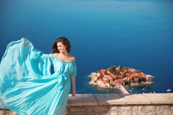 Disfruten. Moda sonriente mujer con soplado vestido sobre azul sk —  Fotos de Stock