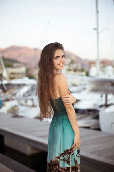 Piękna dziewczyna brunetka uśmiechający się z długimi włosami pozowanie przez jachty — Zdjęcie stockowe