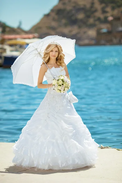 Schönes lächelndes Brautmädchen im Brautkleid mit weißem Regenschirm — Stockfoto