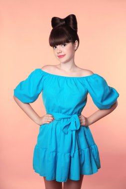 Hairstyle. Beautiful smiling girl with bow hair posing in blue d