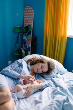 Genç bir kadın yatak odasında bebekle yatakta yatıyor.