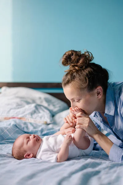 A young mom is kissing a newborn. Motherhood is the happiness of motherhood. New life of the infant at home. Caring feelings love tenderness. The mother admires the child. Happy cute woman and son