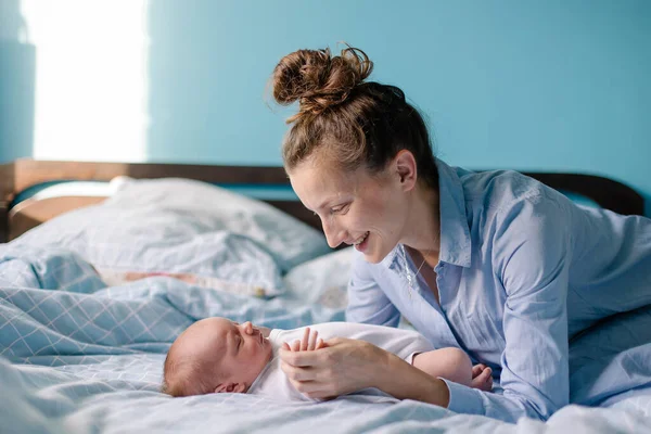 A young mom is kissing a newborn. Motherhood is the happiness of motherhood. New life of the infant at home. Caring feelings love tenderness. The mother admires the child. Happy cute woman and son