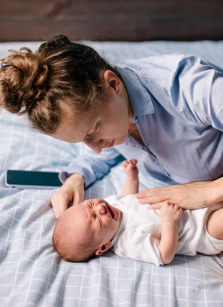 Young tired mother soothing a crying baby. The newborn is crying worried about a sore tummy. Infant colic. motherhood