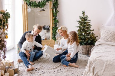 Klasik modern aile Noel 'i selamlıyor. Ebeveynler ve çocuklar yataktalar. Beyaz örülmüş kazaklar. Yeni yıl sabahı. İskandinav iç yatak odası bir çelenkle süslenmiş. Birlikte mutluluk