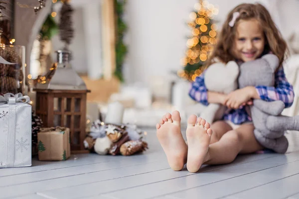 Küçük güzel kız Noel sabahı oturma odasında oyun oynuyor. Mutlu çocukluk haz anları. Yaşam tarzı. Xmas havası. Bir çocuk yeni yılda oynar. Rahat bir oturma odası. Güzel topuklar.