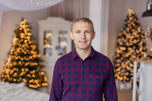 Portrait of attractive middle age man close-up inside in christmas.  short hair blue eyes men in a plaid shirt smiling. Cozy at home in the new year. European appearance Caucasian. happy. Bokeh light