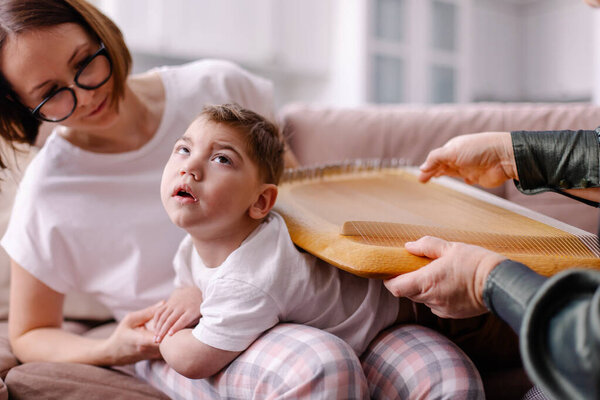 Занимается ребенок с церебральным параличом. Реабилитация инвалида с музыкой. Арт терапия. Реабилитационный терапевт музыкант играет на арфе. Ощущение тактильной вибрации. Ребенок с аутизмом 