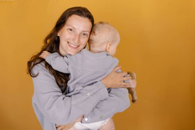 Gri pijamalı anne bebeğe sarılıyor. Anne ve çocuk. Anneliğin mutluluğu. Çevre vejetaryeni. Doğaya yakınlık. Mutlu bir çocukluk. Doğal kumaş. Yeşil arkaplan kopyalama alanı. Yaşam biçimi