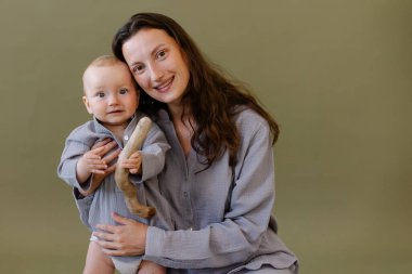 Gri pijamalı anne bir bebeğe sarılıyor. Anne ve çocuk. Anneliğin mutluluğu. Çevre vejetaryeni. Doğaya yakınlık. Mutlu bir çocukluk. Doğal kumaş. Yeşil arkaplan kopyalama alanı. Yaşam tarzı çocuğu