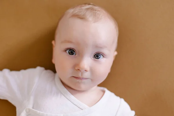 Beyaz elbiseli şirin bir çocuk arka planda oturuyor. 8 aylık çocuk gülümsüyor.. 