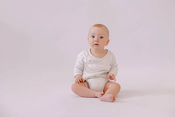 cute little kid in a white bodysuit sits on  background. 8 months old boy smiling.
