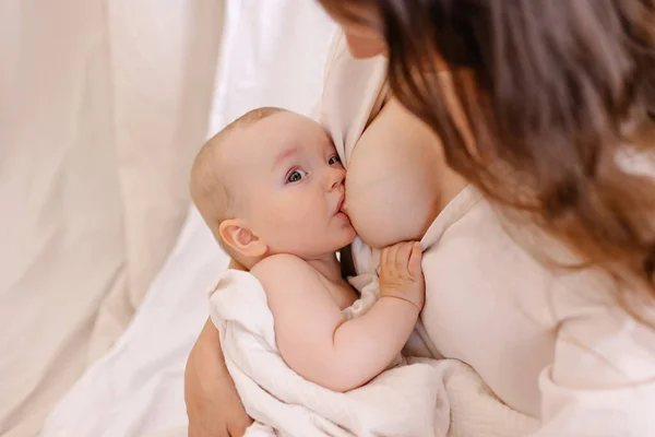 Anne bebeğini emziriyor. Beyazlı kadın ve kollarındaki çocuk. Çocuk anne sütü emiyor. Kutsal annelik. Şefkat koruması. Anne sevgisi kavramı. Doğal beslenme. Çevre ebeveynliği