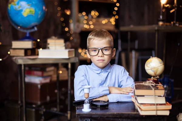 schoolboy puts on glasses. Back to school concept. A boy nerd in a  uniform. Primary School. Home work place. Classroom. Hunger for knowledge. Study education. books and globe table interior