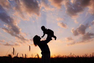 Anne ve bebek gün batımının arka planında tarlada. Ailenin doğaya yakınlığı. Anne sevgisi. Bulutlu şafak vakti. Göz kamaştırıcı manzara arka plan duvar kağıdı. Güzel Annelik