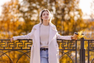 Pozitif kadın parka kahve almaya gitti. Kıyafetlerle sonbahar havası. Merhaba October! Şehre düş. Memnun oldum. Sıcak bir akşam, güneşli bir hava. Dışarıdaki sarışın. çoklu uzay. Şükran Günü